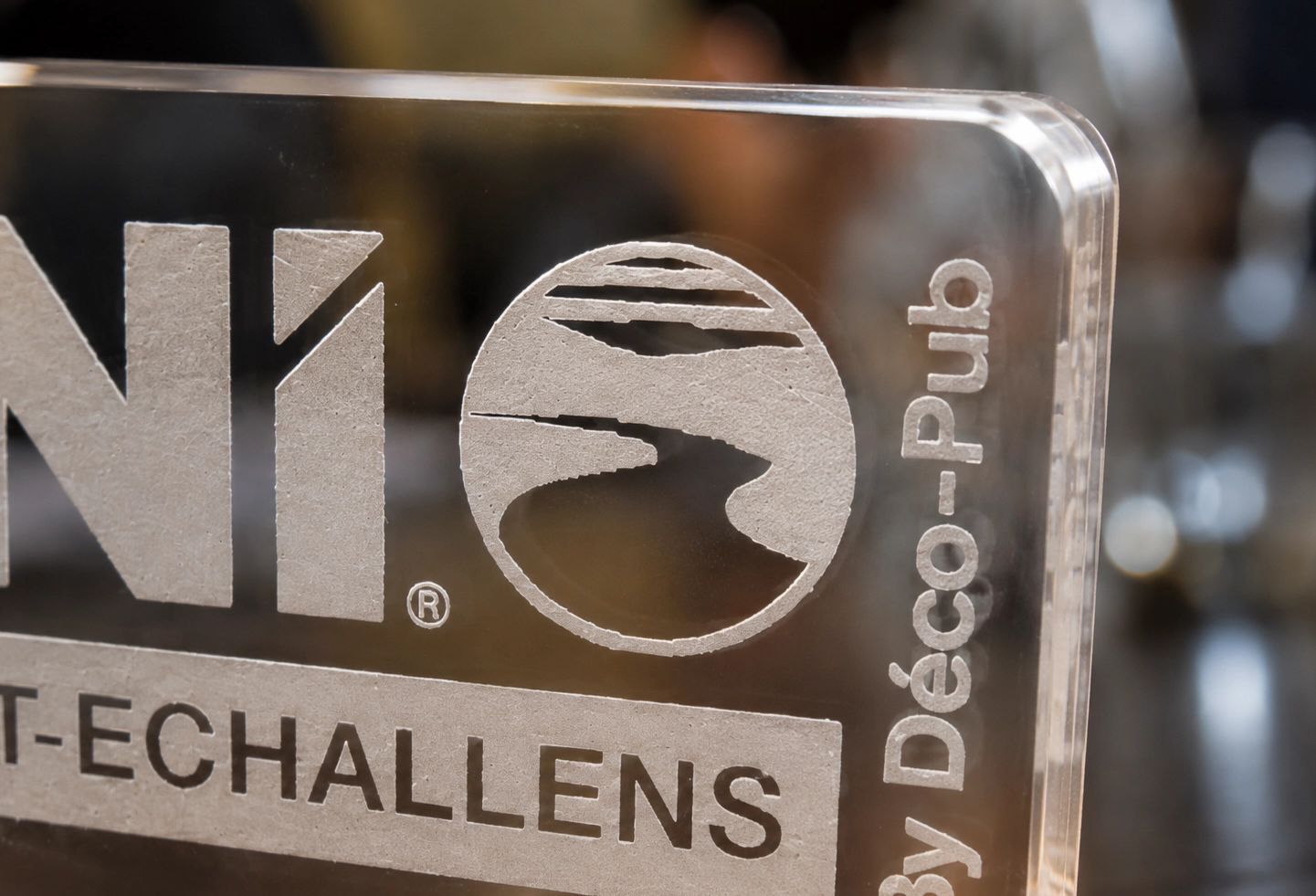 Détail d’une gravure laser blanche sur plaque en plexiglas transparent BNI Talent-Échallens.
