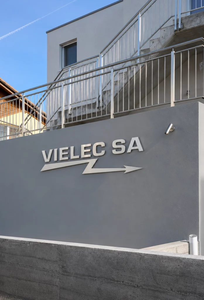 Enseigne en lettres aluminium découpées fixées sur la façade moderne d’une entreprise suisse.