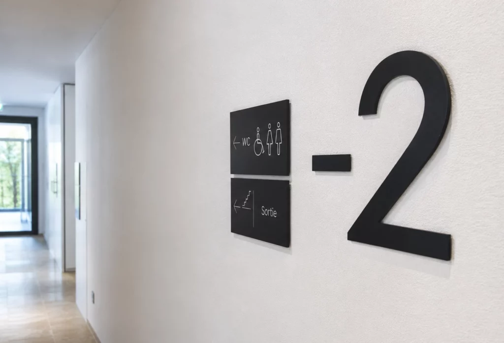 Plaque directionnelle installée près d'un ascenseur pour orienter les visiteurs.