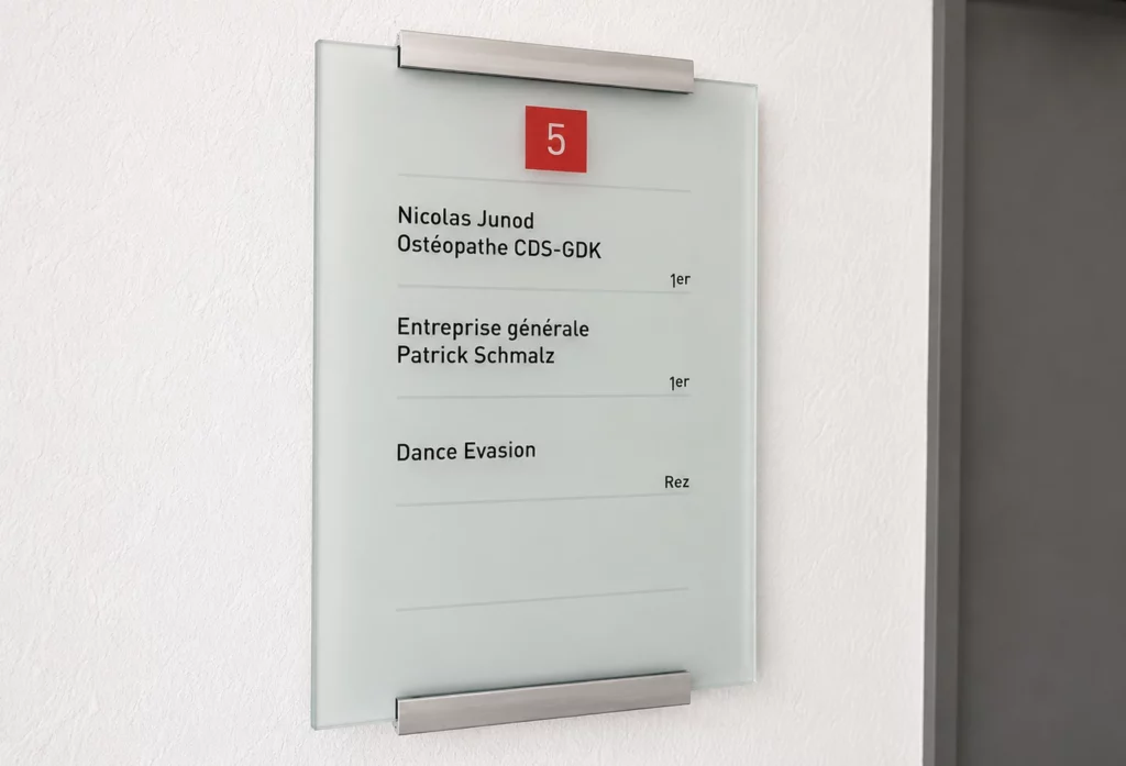 Plaque signalétique en verre avec entretoises inox installée dans les locaux d'une entreprise.